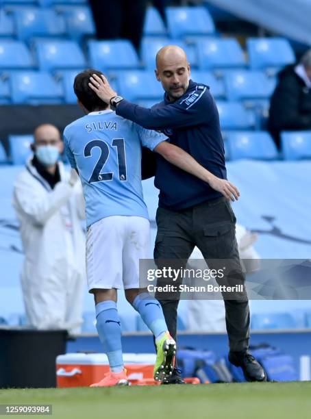 David Silva of Manchester City is greeted by Pep Guardiola, Manager of Manchester City after being substituted on his final performance for...