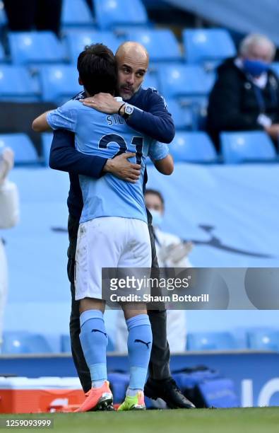 David Silva of Manchester City is greeted by Pep Guardiola, Manager of Manchester City after being substituted on his final performance for...