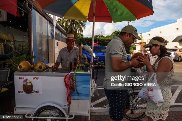 Couple shares their coconut water to cool off from the heat on 8th Street in Little Havana, Miami, Florida during a heat wave on June 26, 2023.