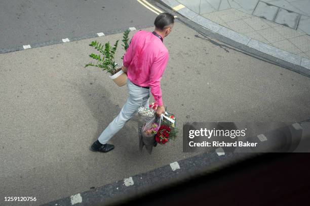 An aerial view of a man wearing a pink shirt and who is sweating from the effort of carrying potted plants and bouquets of flowers in central London,...