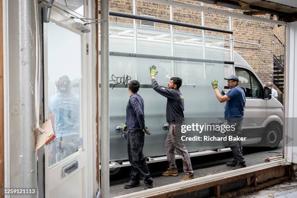 Team of window specialists replace plate glass in a retail business space that's being renovated in Ealing, on 26th June, in London, England.