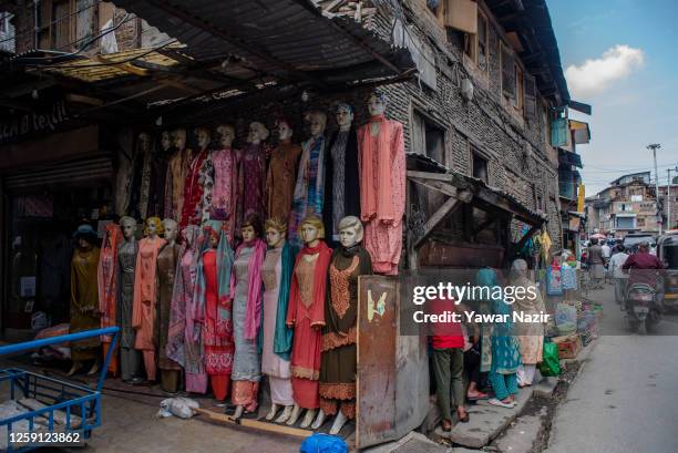 Mannequins adorned with ladies garments hang on a wall of a building as Muslim customers buy goods in a market , before the upcoming Muslim festival...