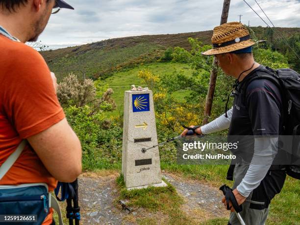 Pilgrim is showing the yellow shell logo to another pilgrim while walking the Camino Primitivo in Galicia, Spain. On May 27th, 2023.