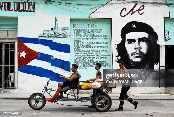 People transport food in a tricycle passing by a wall painted with the Cuban flag and a portrait of Argentine-born revolutionary leader Ernesto "Che"...