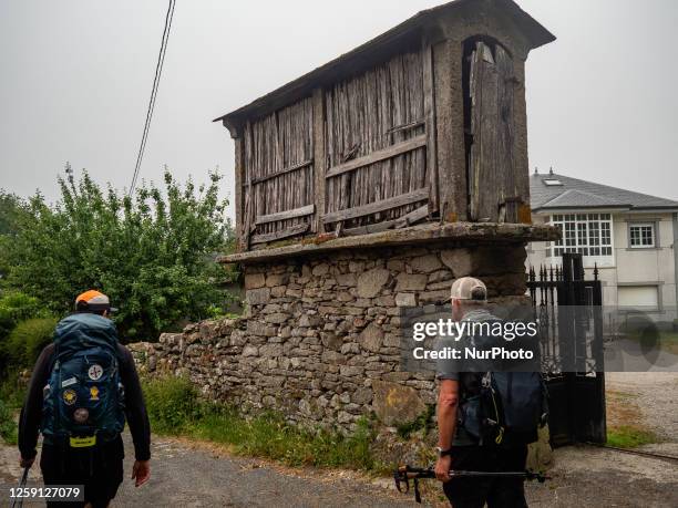 Two pilgrims are seen passing by in front of a traditional horreo while walking the Camino Primitivo. On May 30th, 2023.