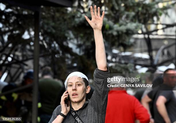 Wounded woman waves while speaking on the phone as rescuers and volunteers work to rescue people from under rubble after Russian missile strike to...