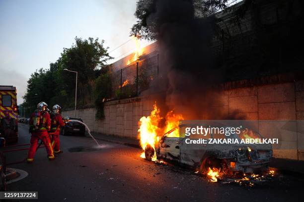 Firefighters work to put out a fire next to a burning car on the sidelines of a demonstration in Nanterre, west of Paris, on June 27 after French...