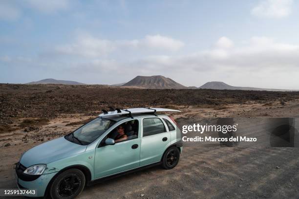 Woman drives a car carrying a surf board though a desert volcanic dirt road north of Fuerteventura Island in the Canary Islands.
