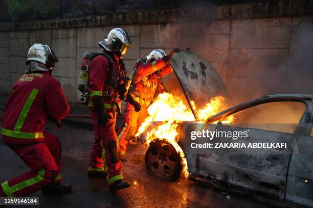 Firefighters extinguish a burning vehicle destroyed by protesters in Nanterre, west of Paris, on June 27 after French police killed a teenager who...