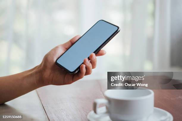 close-up shot of female hand holding a smart phone with blank screen - hand resting on wood stock-fotos und bilder