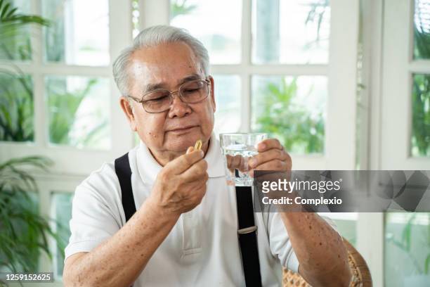 elderly asian man taking pill - fish oil imagens e fotografias de stock