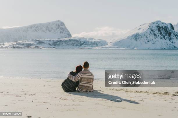 woman and man sitting  on seaside in winter on lofoten island - winter norway stock pictures, royalty-free photos & images