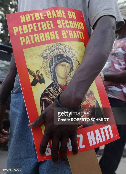 An opponents of Haitian President Jean Bertrand Aristide holds a poster, showing the Virgin Mary holding the infant Christ, prior to taking part in a...