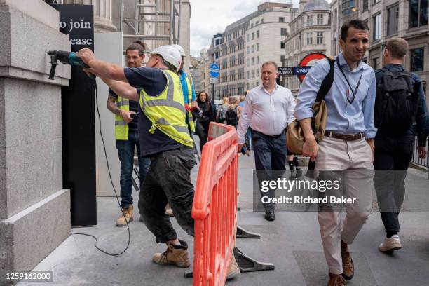 Workman drills into an exterior wall of a construction project as members of the public walk along the street in the City of London, the capital's...