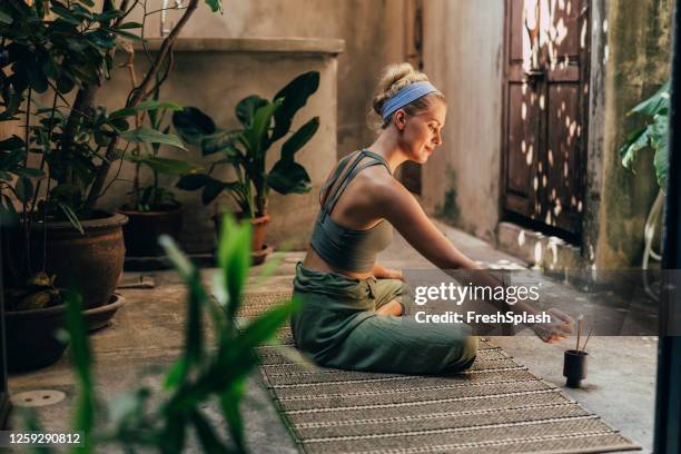 yoga en el jardín: una mujer haciendo yoga mientras disfruta del aroma de los palitos de incienso natural - belleza y salud fotografías e imágenes de stock