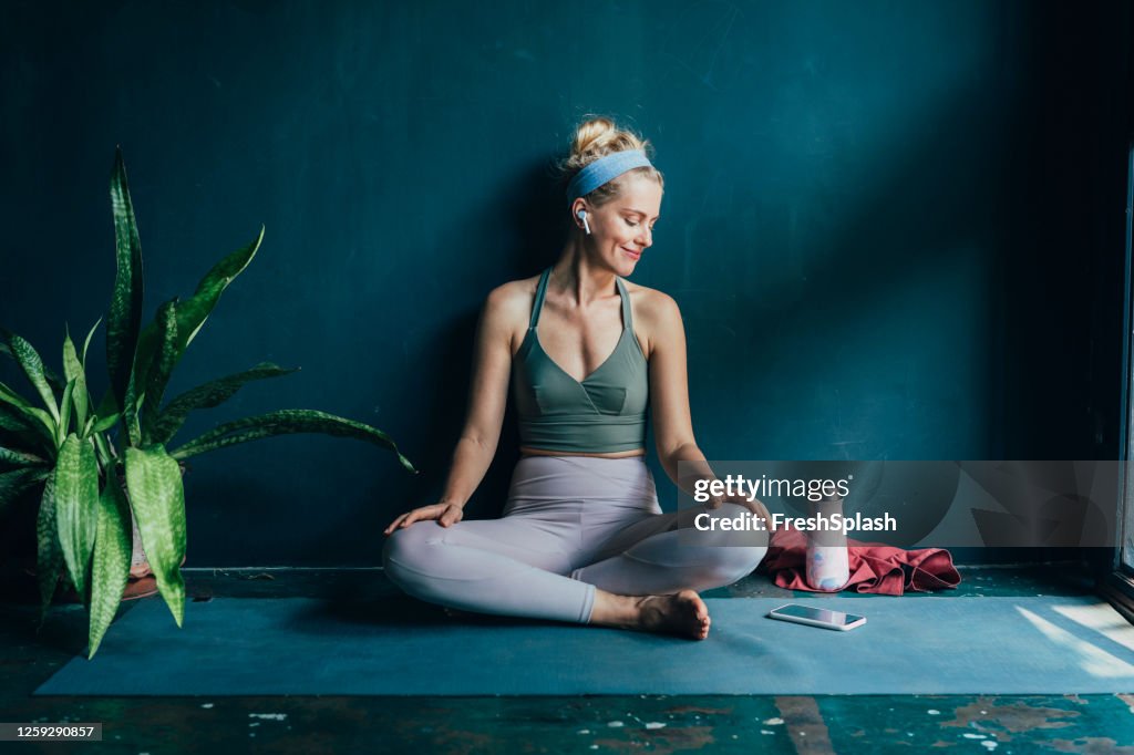 Femme blonde de sourire avec des écouteurs sans fil utilisant son smartphone avant son entraînement à la maison