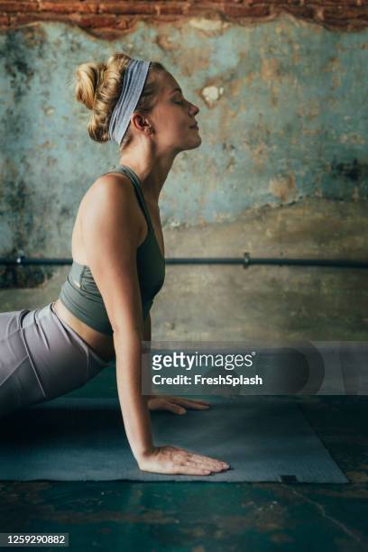 blonde woman in sportswear doing relaxing yoga exercises (asanas) at home - cobra stretch stock pictures, royalty-free photos & images