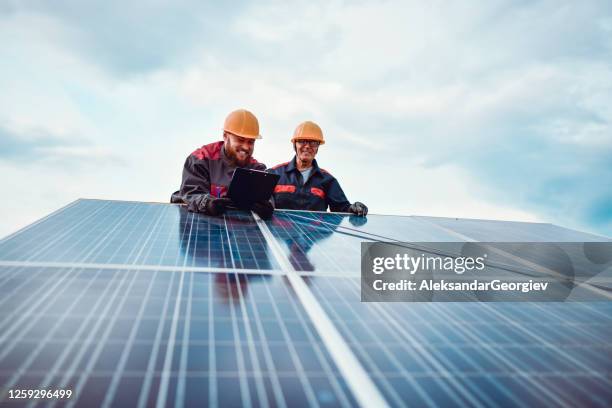 lavoratore anziano che aiuta gli uomini più giovani a misurare le dimensioni del pannello solare - persone fabbrica foto e immagini stock