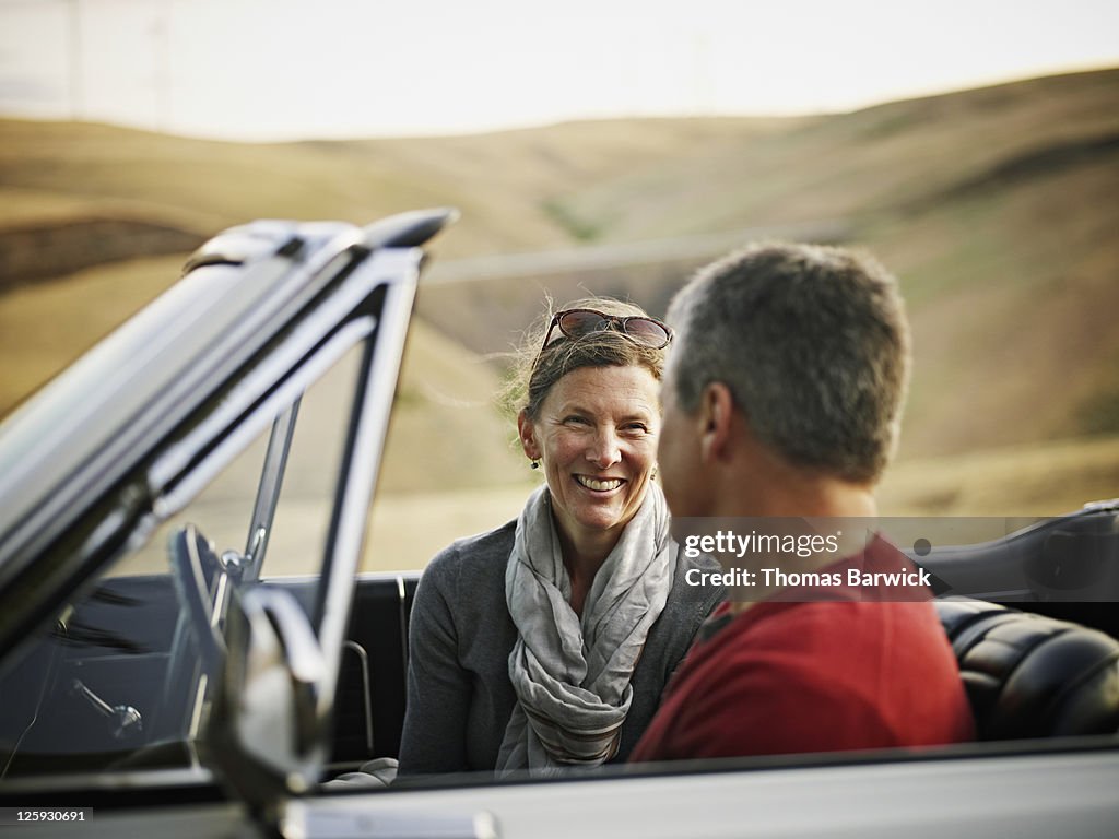 Mature couple sitting in convertible at sunset