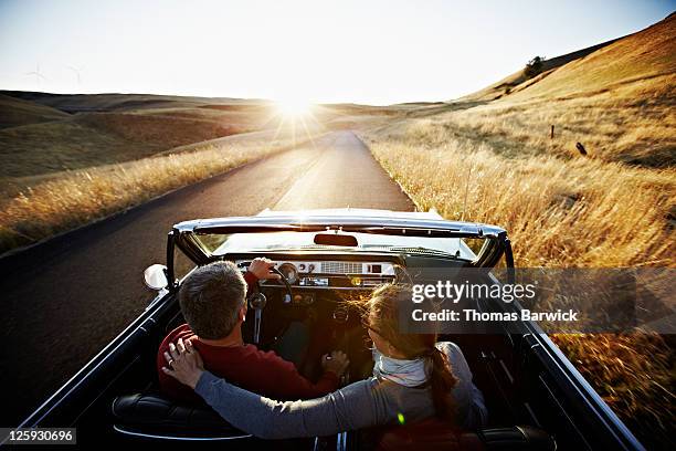 couple driving convertible on empty road at sunset - convertible stockfoto's en -beelden