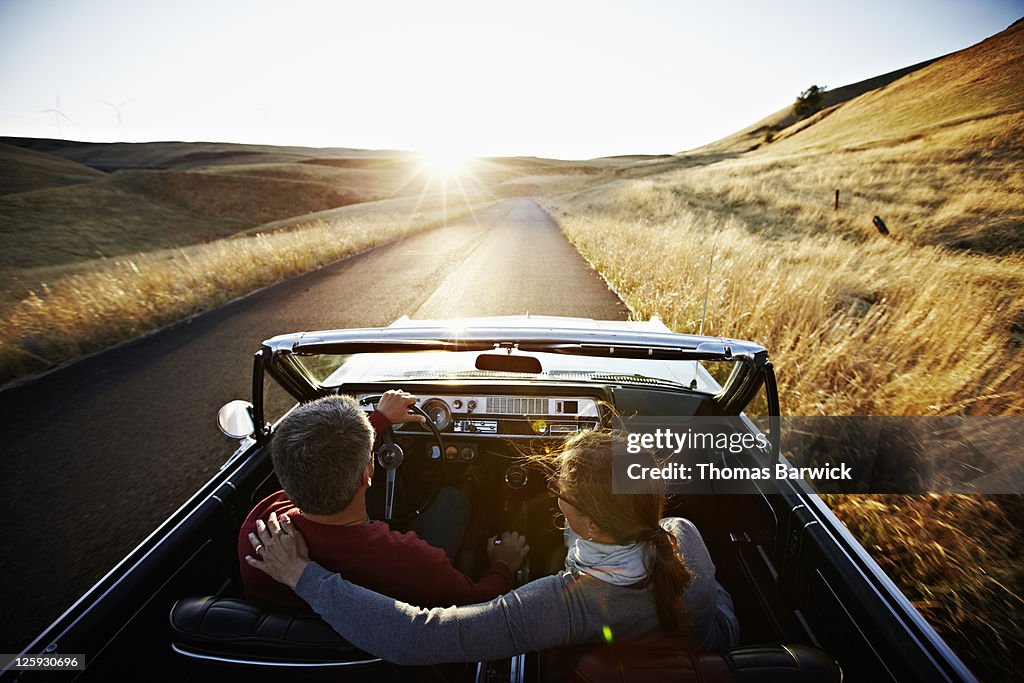 Couple driving convertible on empty road at sunset