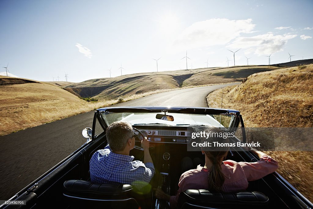 Couple driving convertible in desert at sunset