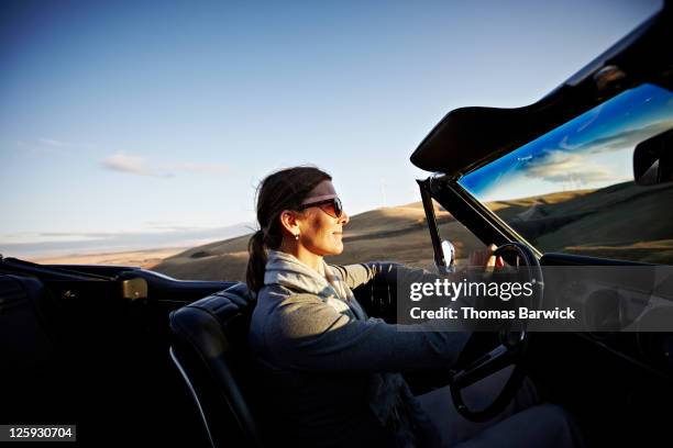 mature woman driving convertible at sunset - convertible fotografías e imágenes de stock