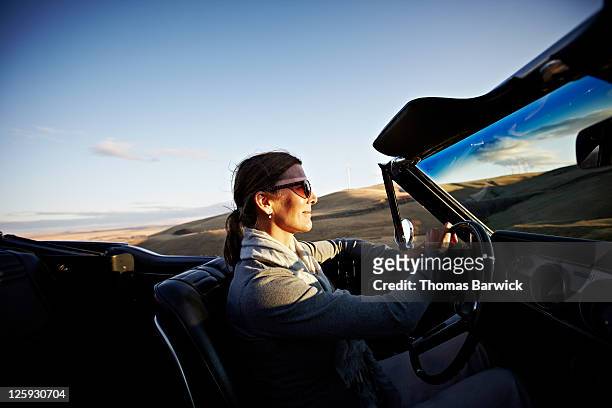 mature woman driving convertible at sunset - convertible imagens e fotografias de stock