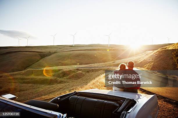 mature couple embracing on car watching sunset - car rear stock-fotos und bilder