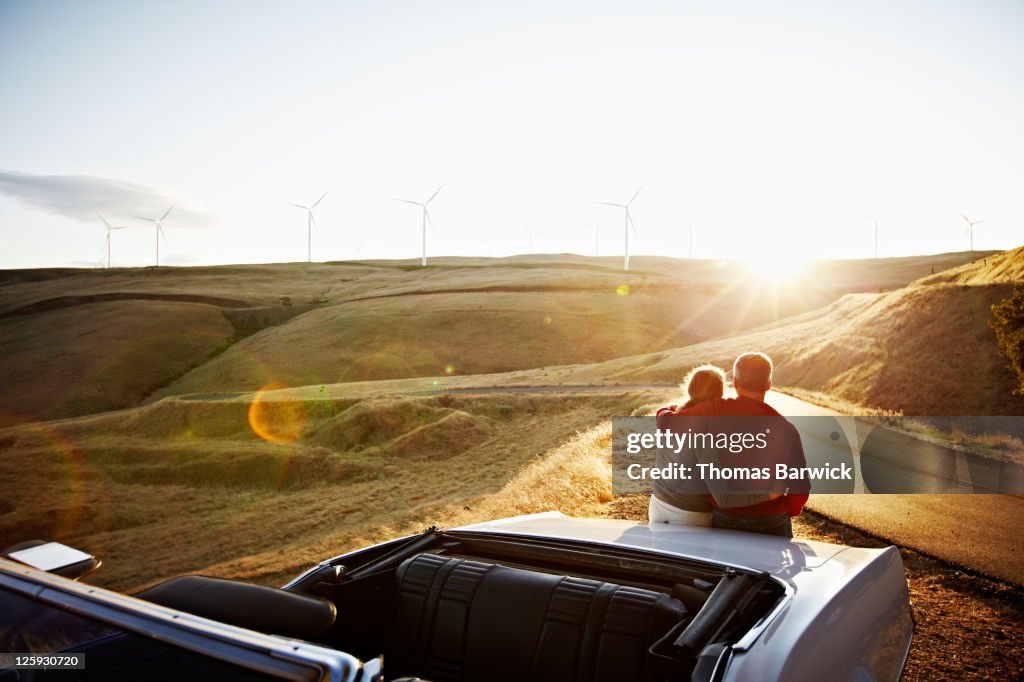 Mature couple embracing on car watching sunset