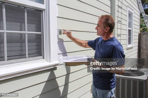 man painting exterior of house holding paint tray - holz streichen stock-fotos und bilder