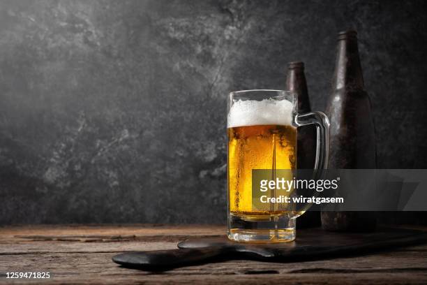 glass of beer on a wooden table with two old bottles. - cereal bar fotografías e imágenes de stock