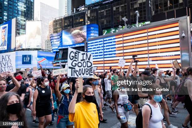 July 26: A protester wearing a mask holds a sign that says, "Get In Good Trouble John Lewis" as the crowd of hundreds pass the Jumbotron of the...