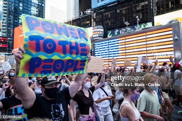 July 26: A protester wearing a mask holds a sign that says, "Power To the People" as the crowd of hundreds pass the Jumbotron of the American Flag in...