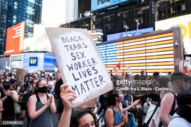 July 26: A protester holds a sign that says, "Black Trans Sex Worker Lives Matter" as the crowd of hundreds pass the Jumbotron of the American Flag...