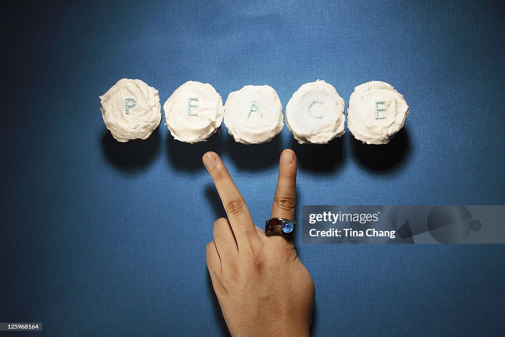 'PEACE' mini cupcakes with a person gesturing a peace sign symbol