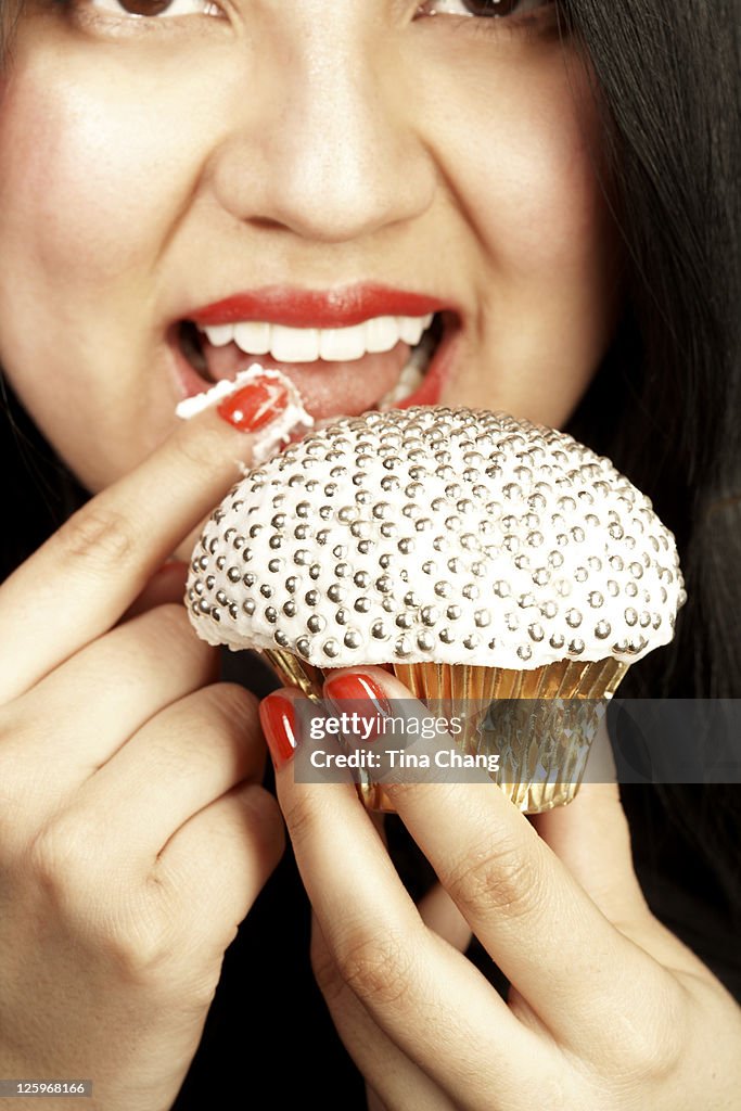 Close-up shot of a young lady tasting the icing of a jewelled cupcake