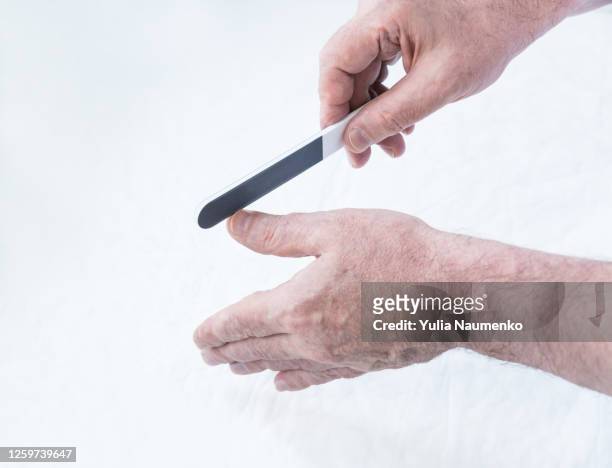 man cutting his nails. making manicure at home. men spa hygiene. hands of an elderly man close-up, a man does a manicure at home, cuts and files nails with a file. - nagelhaut stock-fotos und bilder