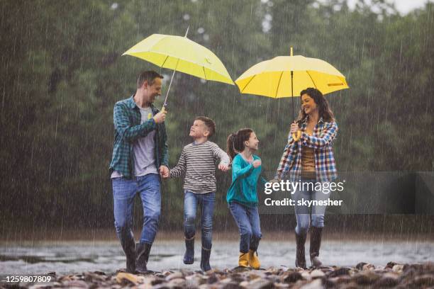 unbeschwerte familie spaßt beim regen am flussufer. - mother protecting from rain stock-fotos und bilder