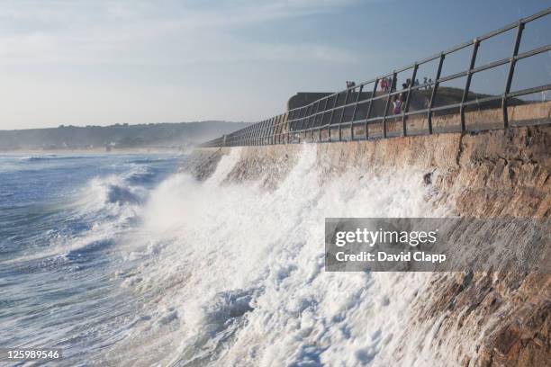 sea wall at st ouen's beach being hit by waves at high tide, jersey, channel islands - zeedijk stockfoto's en -beelden