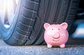 Pink piggy bank sits next to the new tire of a modern car