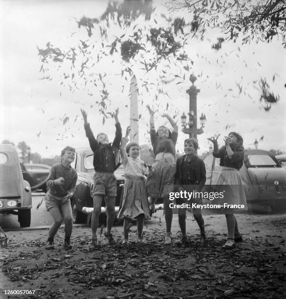 Un groupe d'enfants lance à pleins bras les feuilles mortes devant le jardin des Tuileries, à Paris, France le 23 septembre 1957.