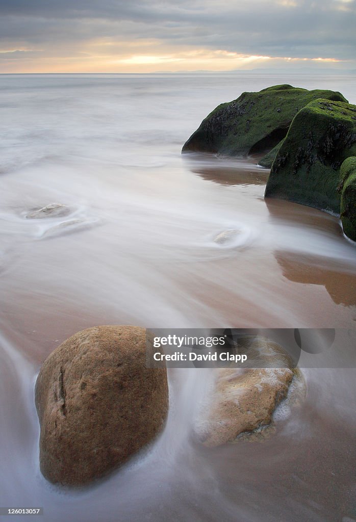 The tide flowing in around rocks on the beach at Rodney Bay near Exmouth in Devon.