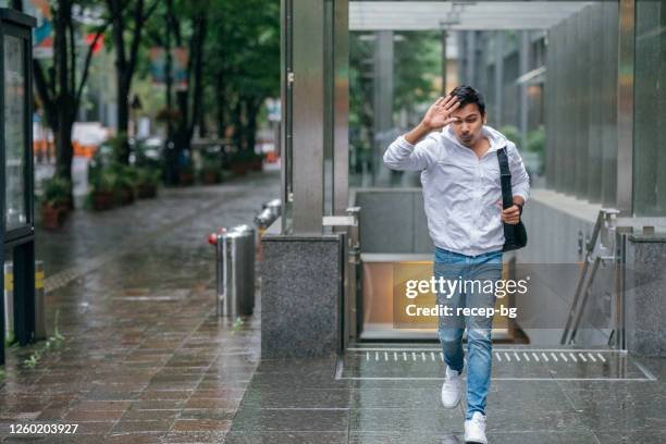young man unprepared for the rain and trying to escape from the rain without umbrella in city - asia rain stock pictures, royalty-free photos & images