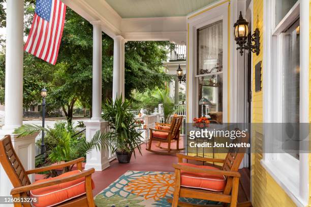 front porch of yellow house with american flag in summer - porch stock-fotos und bilder