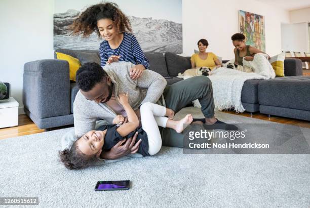 daughters pile on their dad in the family living room - girls wrestling stock pictures, royalty-free photos & images