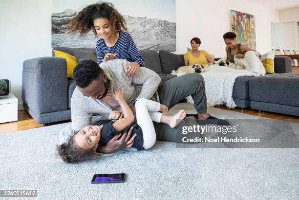 daughters pile on their dad in the family living room - 玩耍式打鬧 個照片及圖片檔