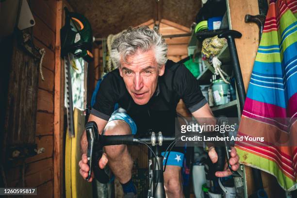 man with determined expression exercising on a static bike in the shed - spandex stockfoto's en -beelden