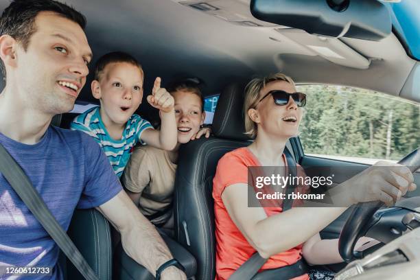 amazing journey of a happy young family with playful children by car during a tourist trip. the little son emotionally points a finger forward. inside view - car rental stock pictures, royalty-free photos & images