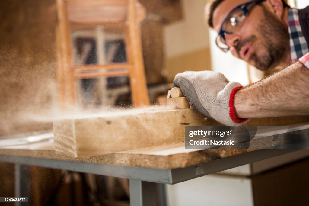 Young carpenter blowing off sawdust while using Sand paper on a plank of wood